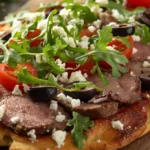 Veal Mea Mediterranean flatbread topped with grilled veal slices, cherry tomatoes, arugula, olives, and feta cheese on a wooden board.