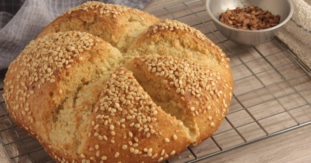 Freshly baked squaw bread loaf on a wooden table, golden-brown crust with a soft, fluffy interior, sliced to show texture, warm homemade bread ready to serve.