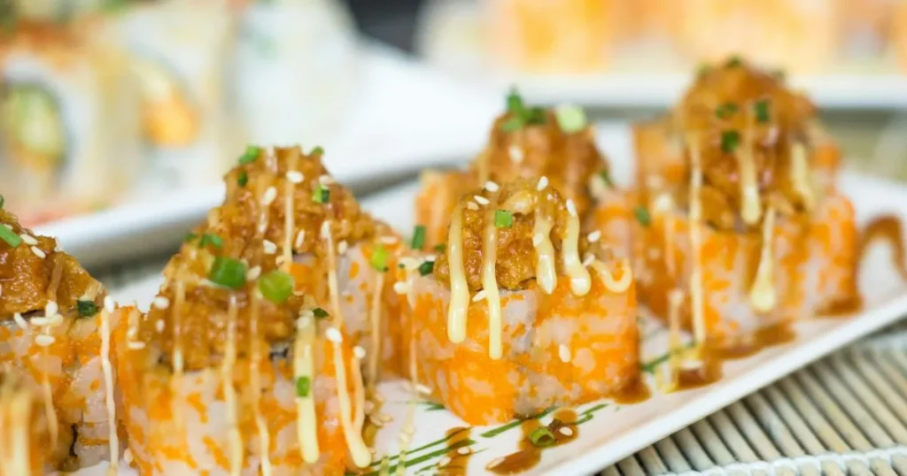 Chopsticks picking up a beef roll wrapped around enoki mushrooms with sauce dripping.