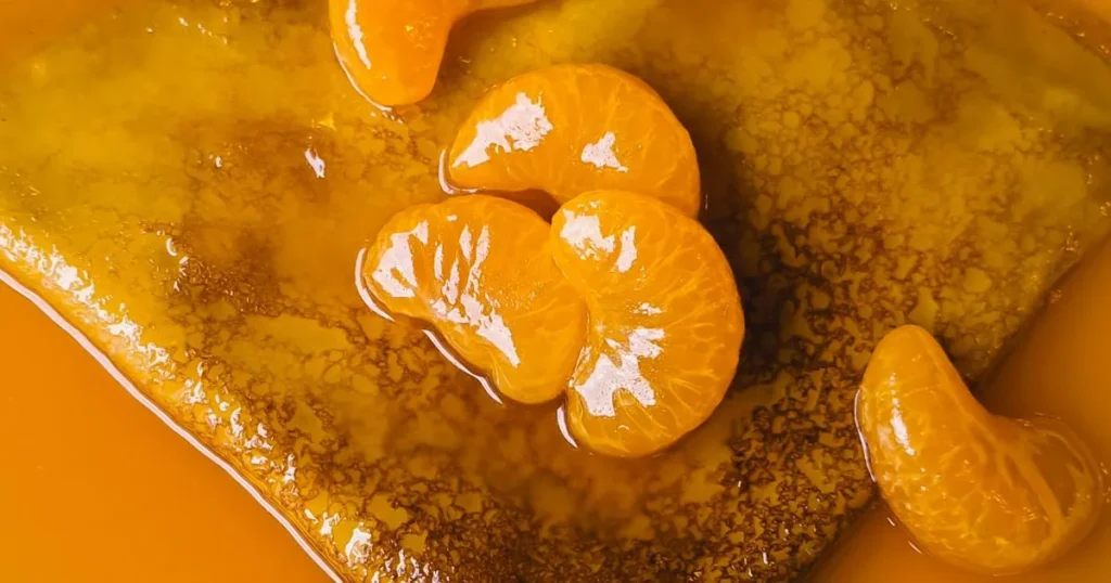 A pan of simmering orange sauce with garlic and ginger being stirred on a stove.