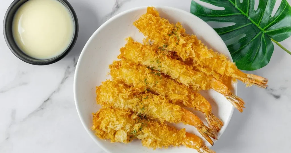 Close-up of crispy tempura being dipped into dark savory sauce with steam rising gently.