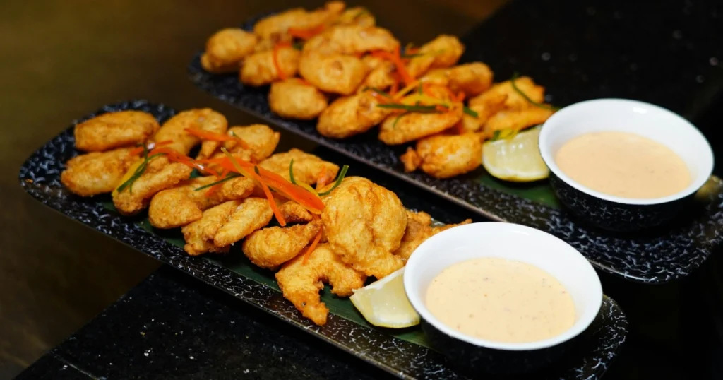 Golden fried tempura pieces arranged neatly with a dipping bowl of Japanese sauce beside them.