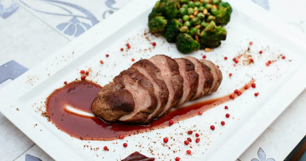 Close-up of pan-seared duck breast sizzling in a frying pan.