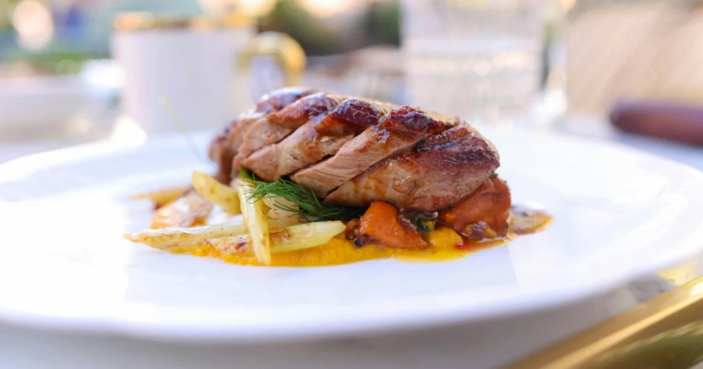 Home kitchen scene showing duck breast cooking in a pan with garlic and sauce ingredients nearby.