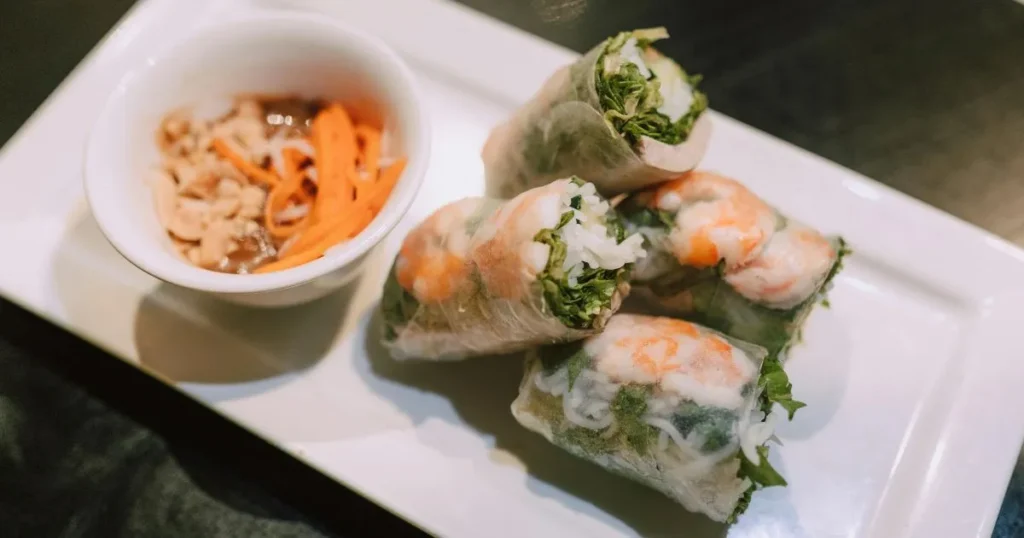 Close-up of spring rolls being dipped into glossy peanut sauce.