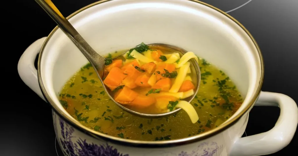 A cozy bowl of steaming soup served with fresh herbs and rustic bread on the side.