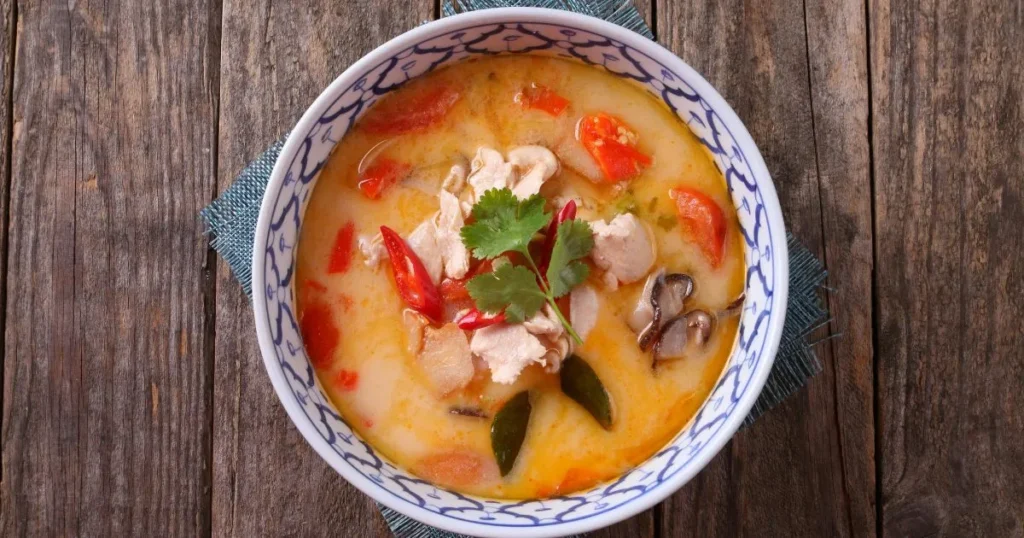 A colorful bowl of vegetable and chicken soup garnished with herbs and lime.