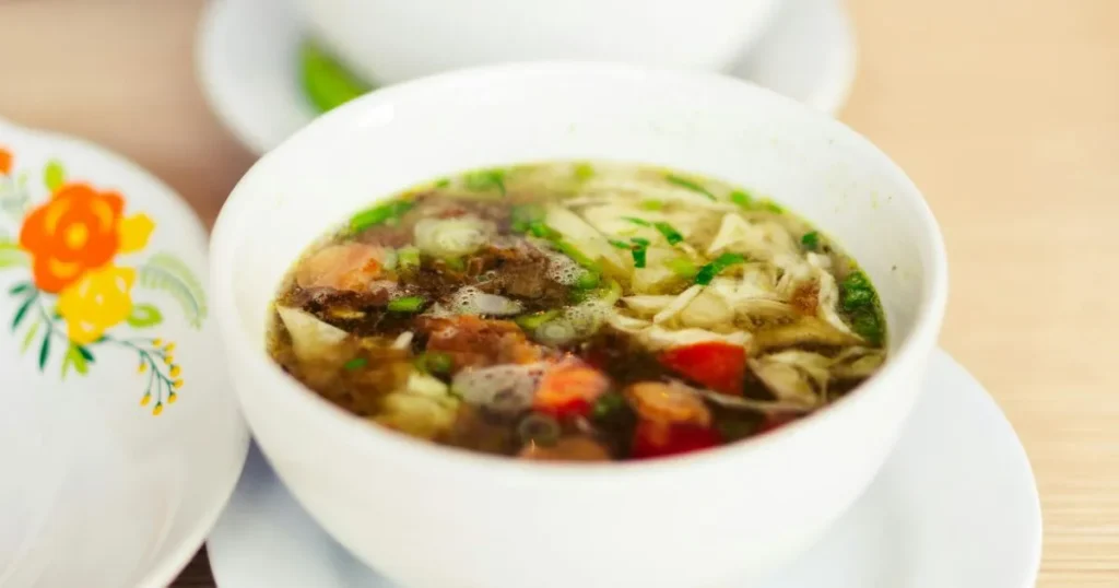 A warm bowl of homemade low sodium chicken noodle soup with carrots, celery, chicken, and egg noodles on a wooden table.