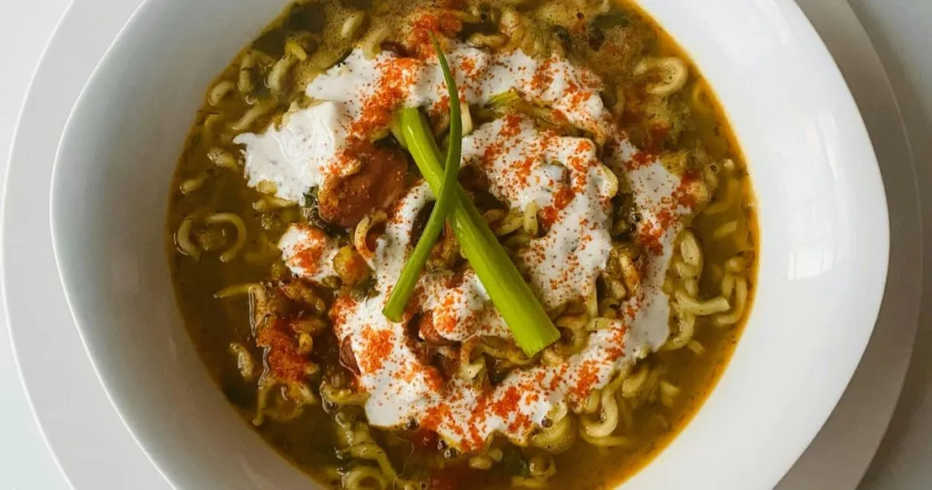 A comforting bowl of low sodium chicken noodle soup with shredded chicken, noodles, carrots, and celery beside fresh herbs.
