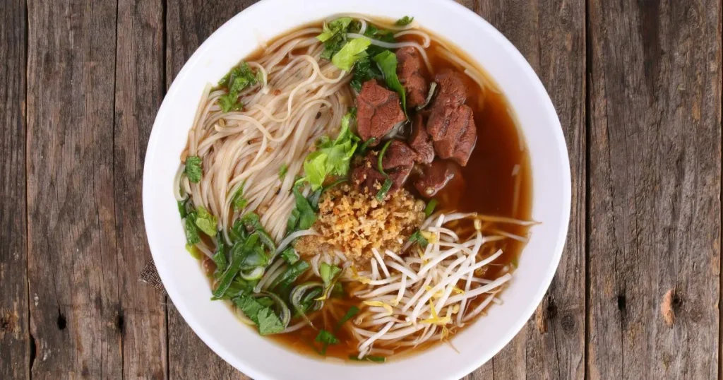 A warm bowl of beef bone soup with carrots, celery, and herbs served beside a rustic loaf of bread.
