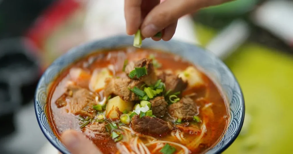 Homemade beef soup bones soup served in a ceramic bowl with vegetables, herbs, and steaming broth.