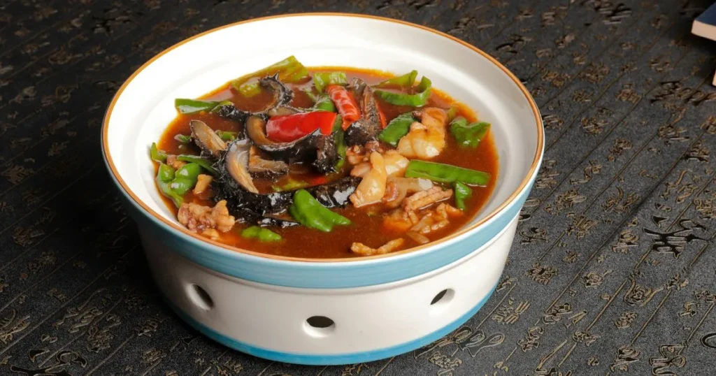 A cozy bowl of sizzling rice soup with crispy rice, mushrooms, carrots, napa cabbage, and green onions on a wooden table.