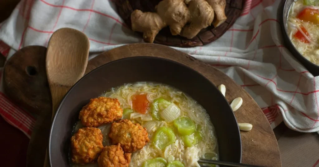 A steaming bowl of homemade sizzling rice soup with crispy rice, chicken, mushrooms, carrots, and green onions beside chopsticks.