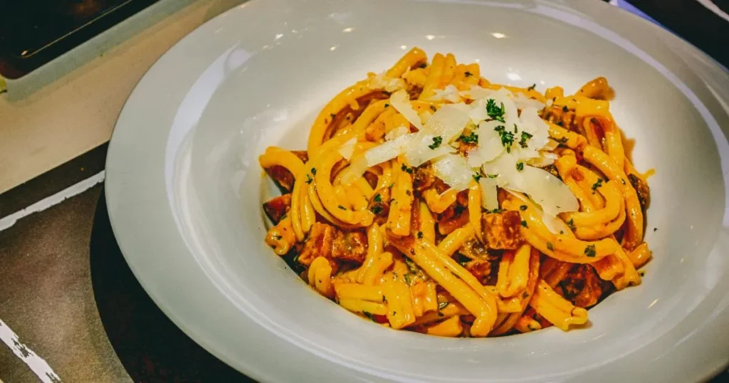 Creamy casarecce pasta served with garlic bread and fresh herbs on a wooden table.