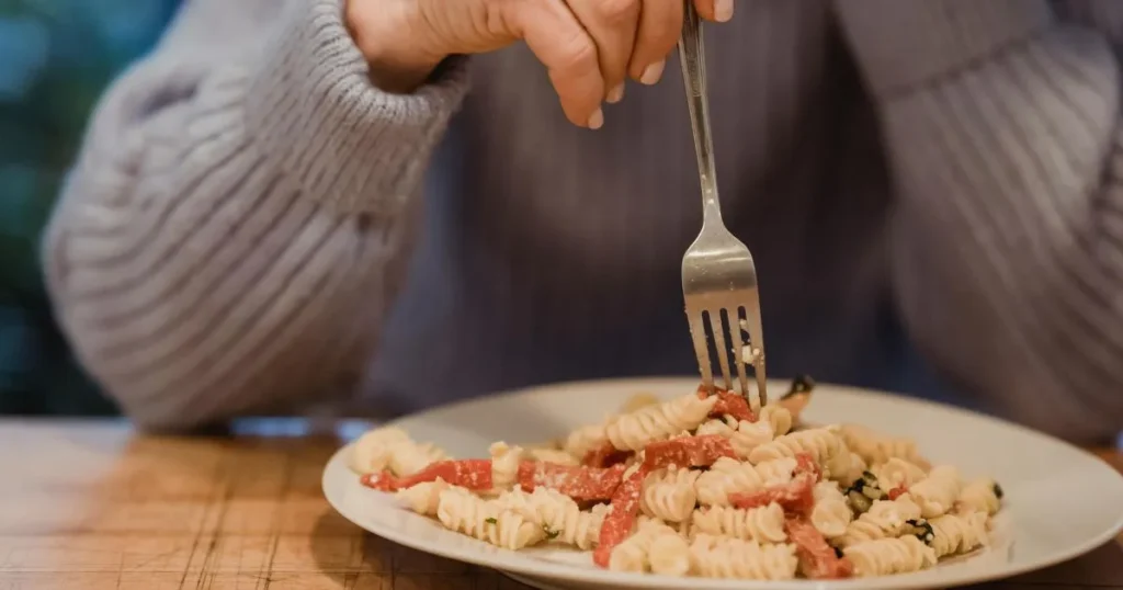 Close-up of radiatori pasta coated in creamy parmesan sauce with browned Italian sausage and fresh herbs.