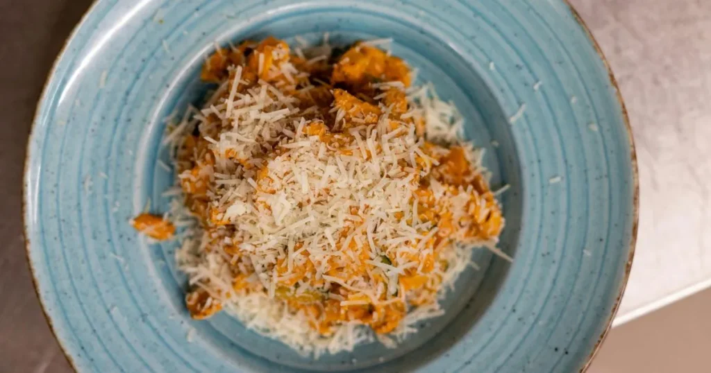 Creamy radiatori pasta with sausage in a skillet topped with parmesan cheese and basil leaves.