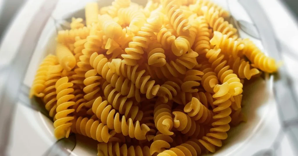 Warm bowl of radiatori pasta mixed with creamy sauce and crumbled Italian sausage on a wooden table.