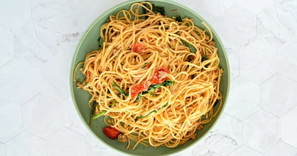 Spaghettini pasta being tossed in garlic butter sauce.
