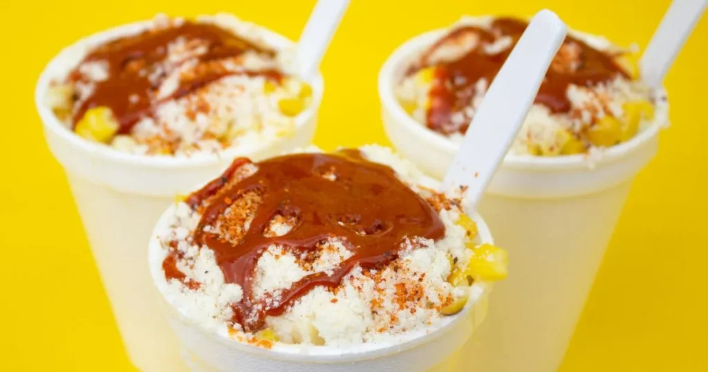 Bowl of creamy pasta with roasted corn kernels, cotija cheese, and lime slices on the side.