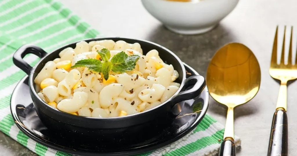 Warm bowl of creamy street corn pasta with charred corn and chili powder garnish.