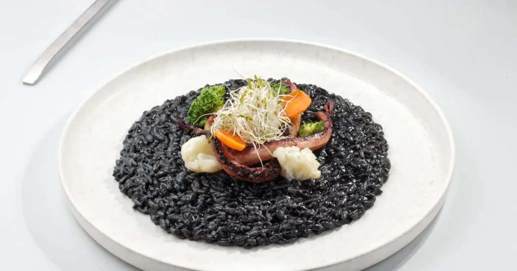 Fresh calamari ink spaghetti coated in garlic butter sauce with seafood and lemon garnish.