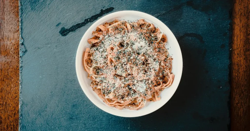 Black calamari ink pasta topped with seafood, parsley, and lemon wedges on a rustic dinner plate.